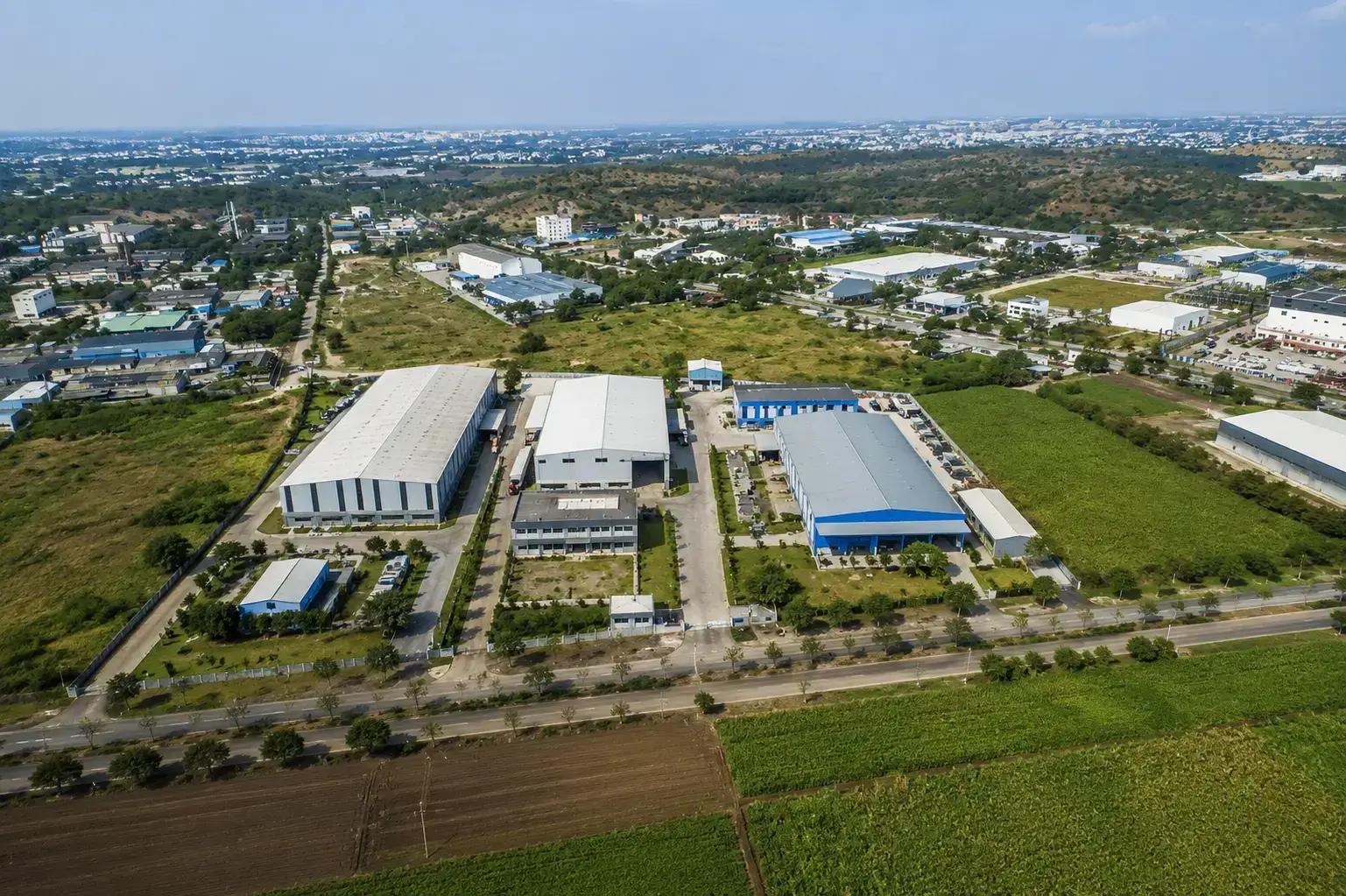 Aerial view of large industrial warehouses and manufacturing facilities surrounded by greenery in the Markal industrial area near Pune.